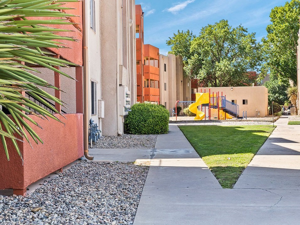 a sidewalk leading to an apartment building with a yellow slide in the background